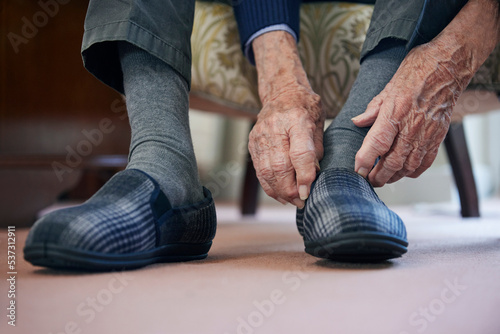 Close Up Of Senior Man Putting On Slippers To Keep Feet Warm In Cost Of Living Crisis photo