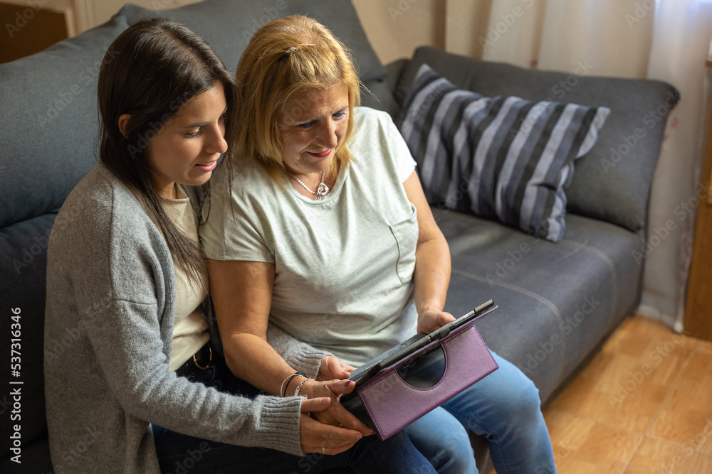 Mother and daughter on the sofa at home while looking at the tablet and being happy. Mother and daughter on the sofa at home while looking at the tablet and being happy.