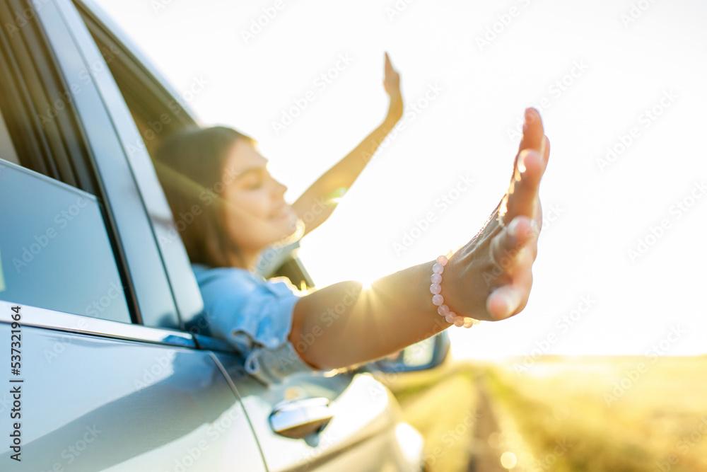 Happy young woman looking out of car window at golden sunset in field