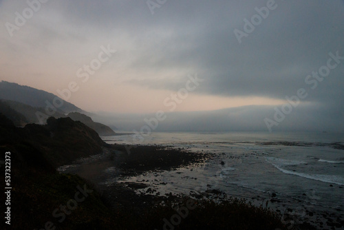 Thick mist coming from the ocean. Seacoast view with cliffs and rocks and thick clouds during twilight