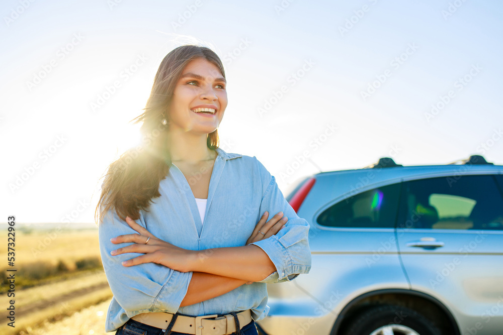 Attractive young woman in blue shirt at sunset light with her car