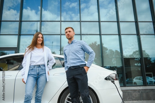 Smiling man and woman on the charging station for electric cars. A man is charging a car. © Serhii