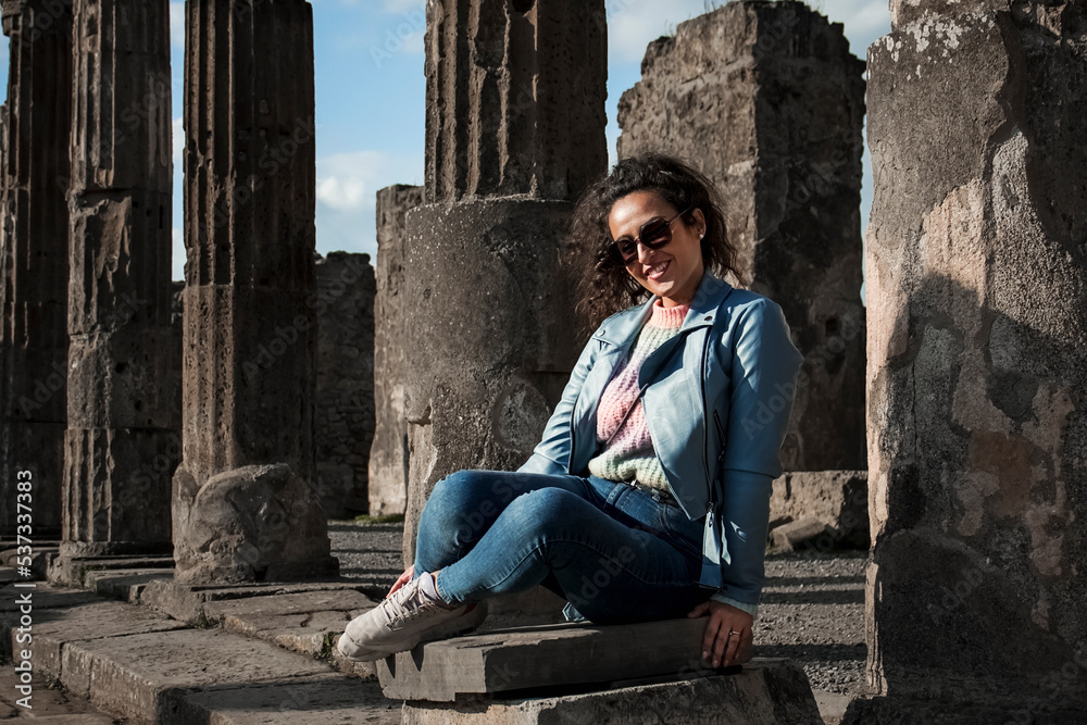 beautiful Mediterranean woman with curly hair posing in the ancient city of Pompeii, destroyed by Vesuvius during the eruption of 79 AD.