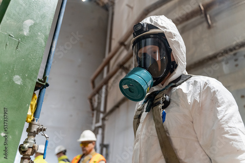A worker in special chemical protective clothing stands in front of a tank of cyanide. photo
