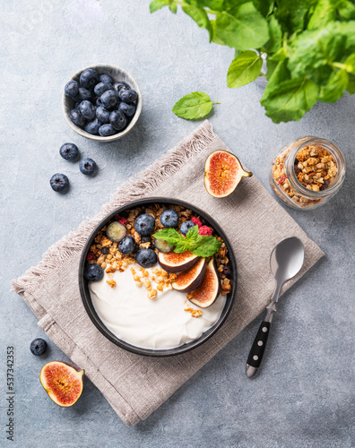 Natural yogurt with muesli, berries and figs  in a black bowl on a blue background with mint. Healthy and nutritious breakfast