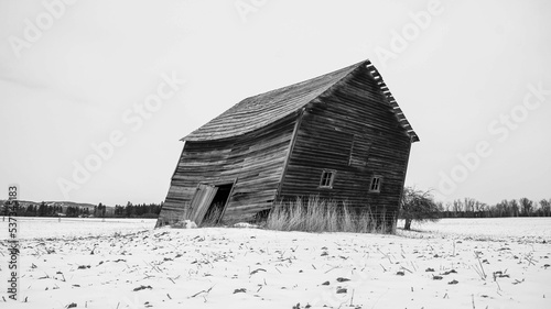 Grayscale shot of a crooked wooden old country house on a field covered in snow