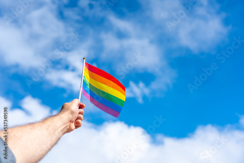 Man s hand with an unfurled LGBT flag on a blue background