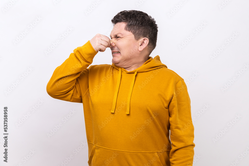 Middle aged man holding breath and grimacing in disgust, expressing repulsion to stink, fart gases, intolerable odor, wearing urban style hoodie. Indoor studio shot isolated on white background. Middle aged man holding breath and grimacing in disgust, expressing repulsion to stink, fart gases, intolerable odor, wearing urban style hoodie. Indoor studio shot isolated on white background.