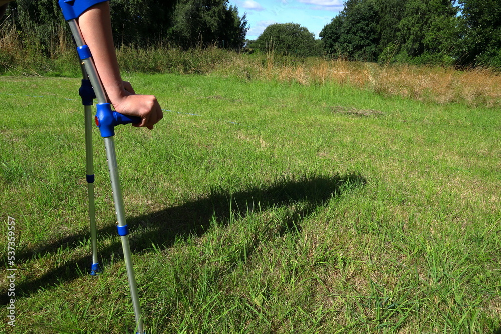 Kid with crutches on a green lawn. Using crutch to walk after one accident. Summer time. Sweden, Europe.