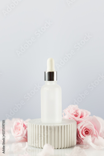 Glass dropper bottle with serum on marble podium with tender pink roses and rose petals. Natural beauty product based on rose flowers  fermented cosmetic. Soft focus style  copy space  vertical format