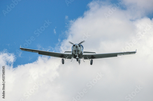 A single-engine plane is flying in the sky among the clouds. A light-engine plane in the blue sky flies through the clouds.