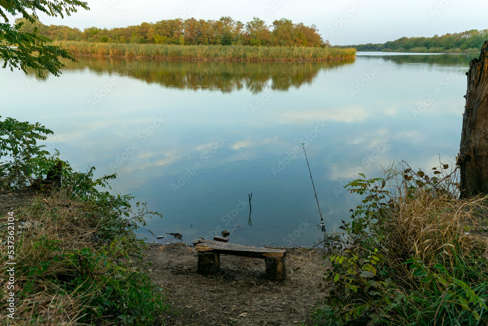Scenic view of a beautiful view in the early morning over a pond or lake against a cloudy sky and reed grass in the foreground. Landscape. Reflection in the water. Fishing, travel, recreation. Scenic view of a beautiful view in the early morning over a pond or lake against a cloudy sky and reed grass in the foreground. Landscape. Reflection in the water. Fishing, travel, recreation.