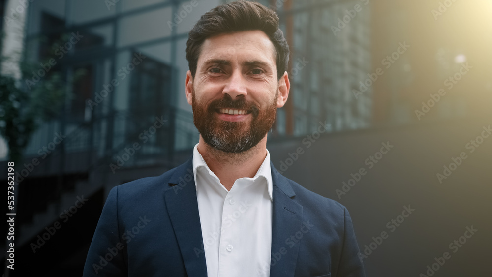 Fototapeta premium Elegant successful caucasian businessman wearing formal suit happy male portrait of adult 30s employee bearded middle eastern attractive man posing outdoors modern city office background in sunny day