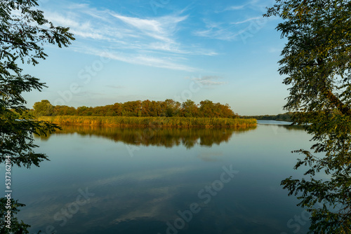 Scenic view of a beautiful view in the early morning over a pond or lake against a cloudy sky and reed grass in the foreground. Landscape. Reflection in the water. Fishing, travel, recreation.