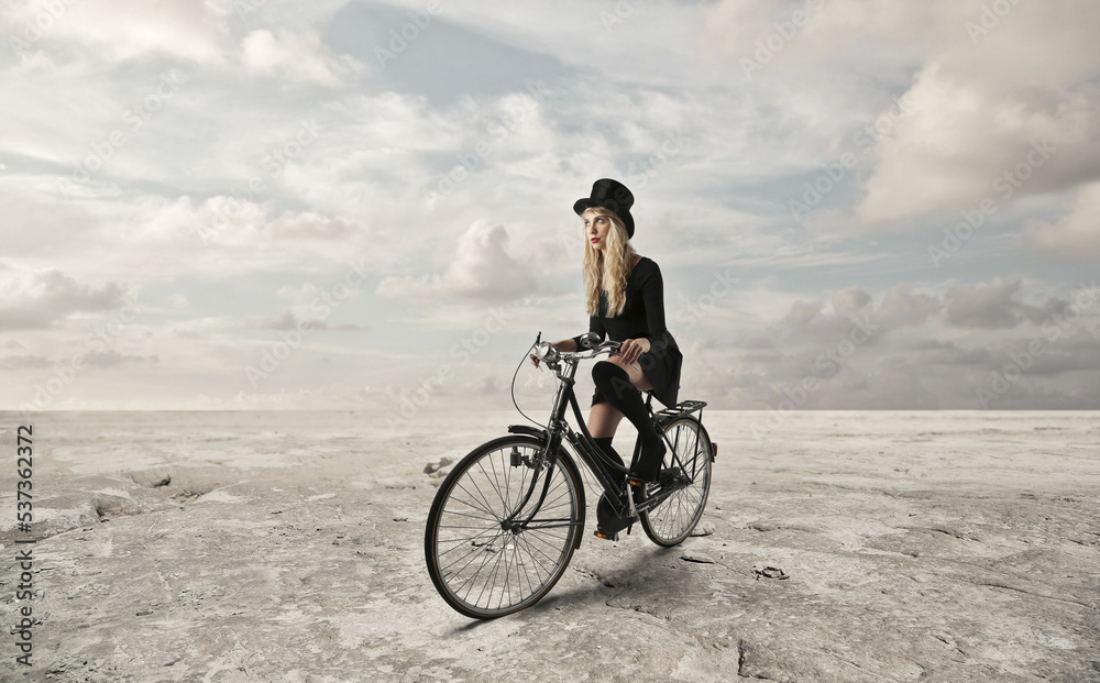 Obraz premium young woman with top hat travels by bicycle in the middle of a desert
