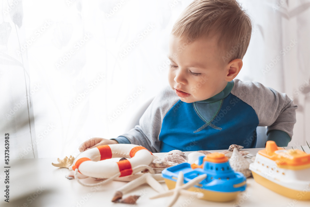 Child play with sea shells and boats. Summer vacation and travel concept. Kid play with lifebuoy and starfish Child play with sea shells and boats. Summer vacation and travel concept. Kid play with lifebuoy and starfish