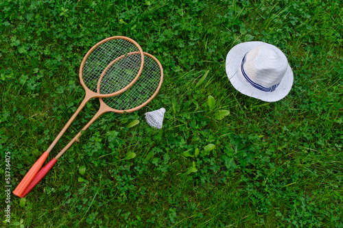 Badminton rackets, a shuttlecock and a hat lie on a green lawn. The concept of active recreation, outdoor games.Top view