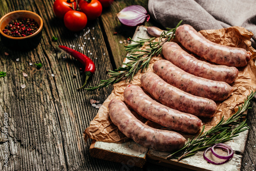raw breed butchers sausages in skins with herbs and rosemary on a wooden background. Sausages for grilling. banner, menu, recipe place for text, top view