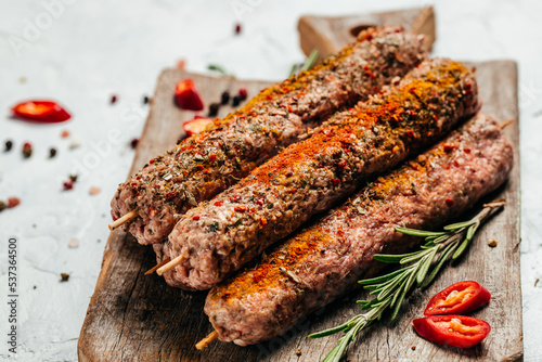 raw Lula kebab on skewers with spices on plate wooden board on a light background. place for text, top view