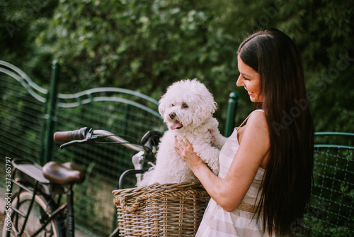 Fotografie Young woman with white bichon frise dog in the basket of electric bike