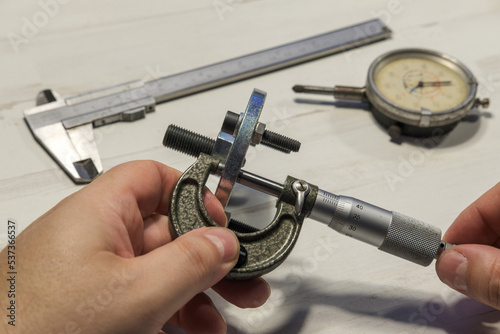 Manos de mecánico midiendo de espesores con micrómetro donde se aprecian además un calibre pie de rey y un reloj comparador