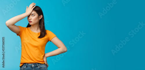 Annoyed arrogant asian girl punch forehead make facepalm sign, roll eyelids irritated pissed, cannot stand lame talks look disappointed ingorant, unwilling to listen, stand blue background photo