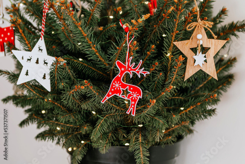 Christmas tree with different wooden decorations. Christmas garland and Christmas lights. White and red colors. Christmas deer, star, snowflake, Bullfinch (ID: 537371507)