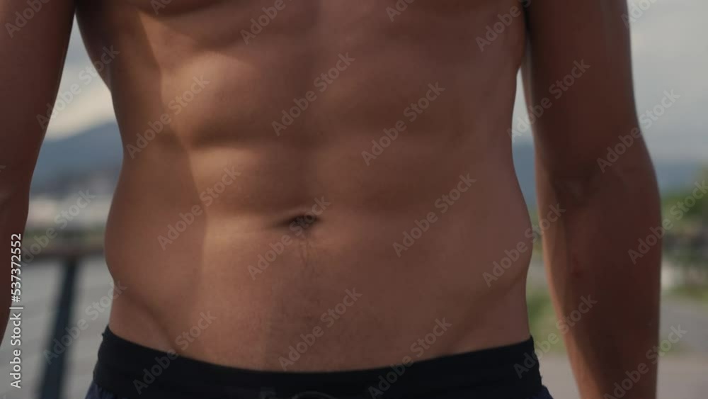Athletic Caucasian man walking topless on the seashore after workout. Front view of young sportsman walking by wet sand on beach with elastic band. Man's beauty concept. High quality 4k footage. Athletic Caucasian man walking topless on the seashore after workout. Front view of young sportsman walking by wet sand on beach with elastic band. Man's beauty concept. High quality 4k footage.