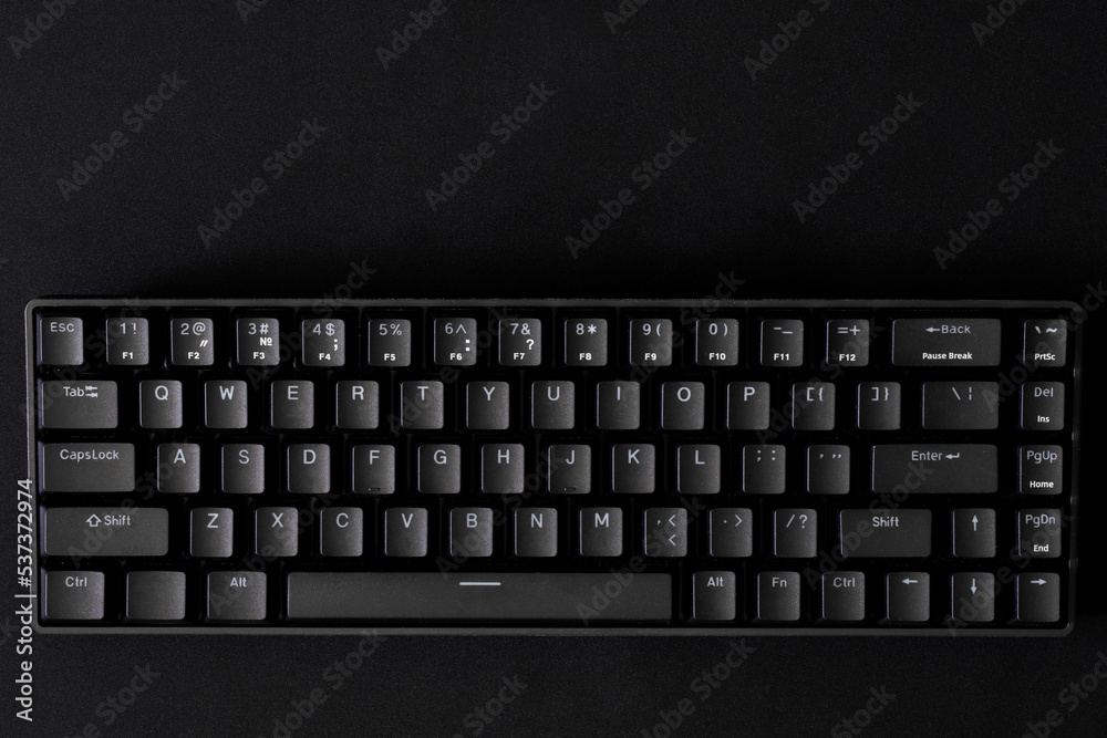 Black mechanical computer keyboard on a black background. Small gaming keyboard with reduced interface and 68 keys - keycaps. Copy space. View from above. Black mechanical computer keyboard on a black background. Small gaming keyboard with reduced interface and 68 keys - keycaps. Copy space. View from above.