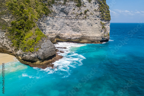 Nusa Penida Island, Kelingking Beach. Top view aerial view of a sandy clean beach with clear blue and turquoise water. Rocks and waves with white foam