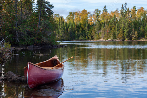 Fotografiet Red wooden canoe on the shore of a Boundary Waters lake in morning light during