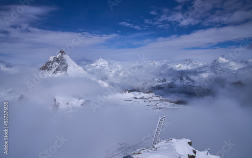 Iconic summit Matterhorn viewed from Klein Matterhorn platform on a sunny cold day. Construction work around the platform. Unusual landscape with a ladder at foreground. Panoramic view above clouds.