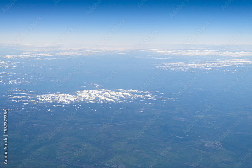 Aerial shot of snowy forested mountain tops, with blue sky