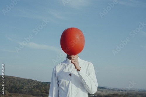 Person holding a red balloon in front of his face photo