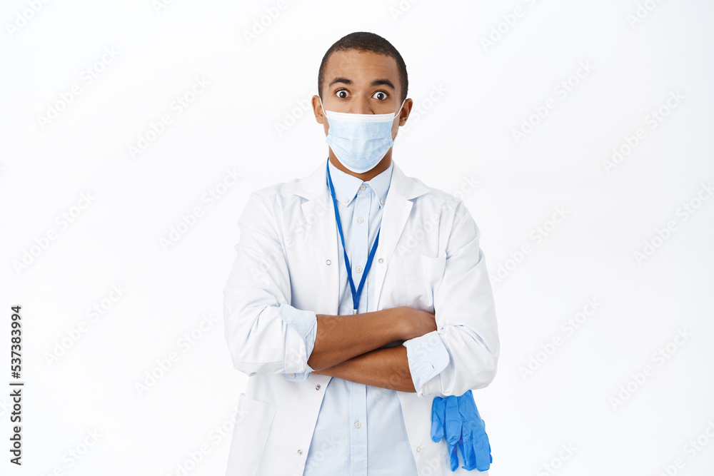 Doctor in medical mask looking surprised at camera, standing over white background Doctor in medical mask looking surprised at camera, standing over white background