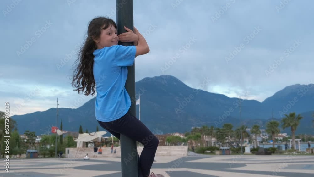 Child climbing a pole in the street. A view of little girl want to