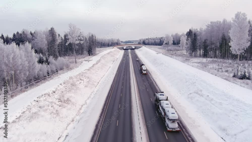 Tallinn.Estonia-February 4.2022: Aerial shot of a highway in Estonia during the cold wintertime. Snowy forest and ground. Cars driving. Cloudy weather. Drone slowly moving forward. Tallinn.Estonia-February 4.2022: Aerial shot of a highway in Estonia during the cold wintertime. Snowy forest and ground. Cars driving. Cloudy weather. Drone slowly moving forward.