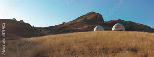 Modern glamorous camping in the autumn mountains of Dagestan. A group of futuristic hotel geodesic domes tents in the middle of a dry grass meadow in the Khunzakh region.