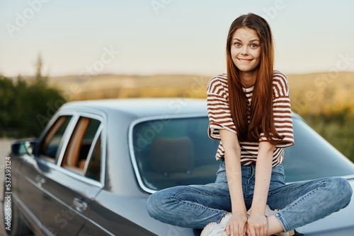 A young woman sits on the hood of her car and laughs with her eyes closed, a journey from a noisy city to nature in summer, Travel lifestyle © SHOTPRIME STUDIO