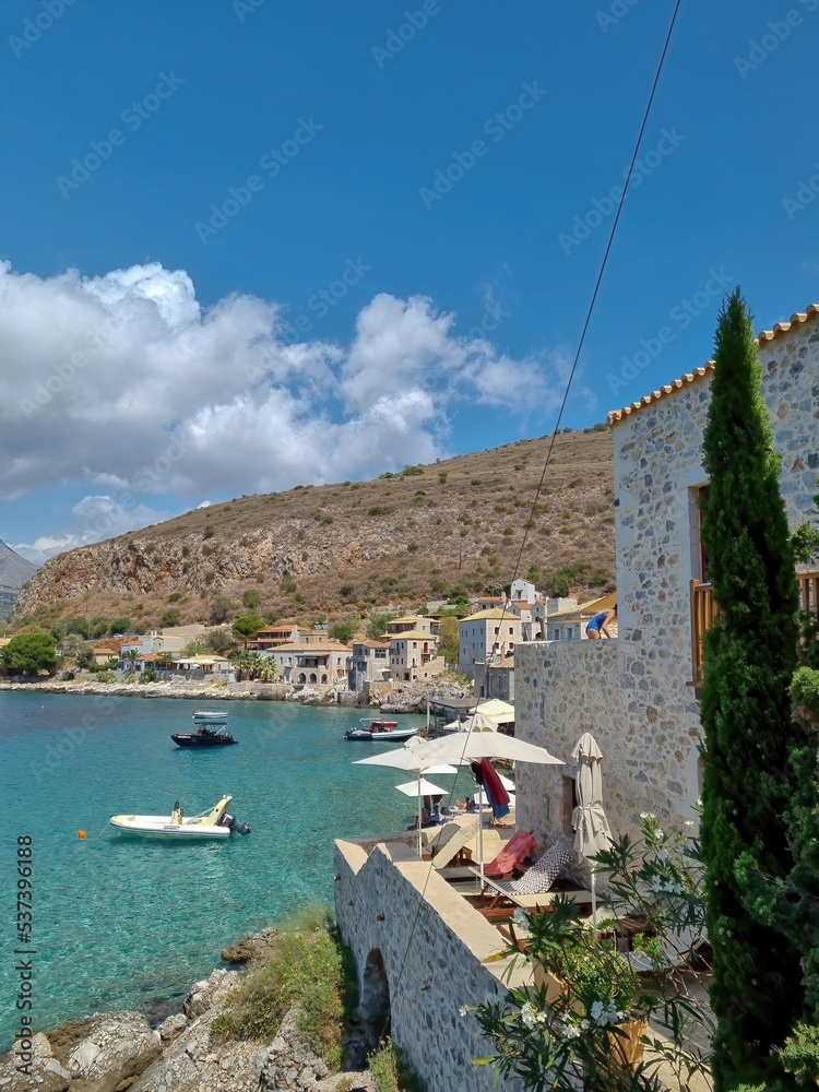view of Limeni village with fishing boats in turquoise waters and the stone buildings as a background in Mani, Greece.