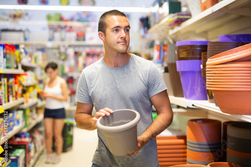 Portrait of modern young adult man choosing pots for house plants in supermarket..