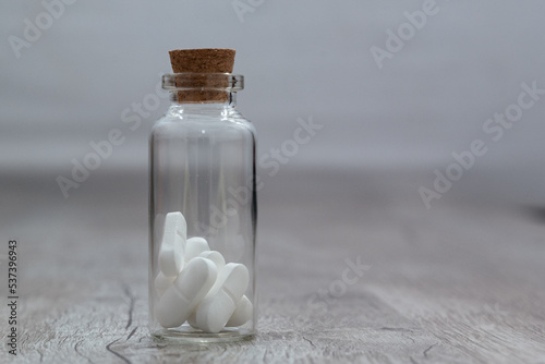 Glass vial with white pills on a wooden table. the Container on a grey background. 