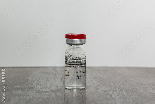 An pharmacy ampoule with drug  for a pandemic cure on the wood table. The ampoule is centered on a light background.