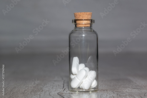Glass vial with white pills on a wooden table. the Container on a grey background. 
