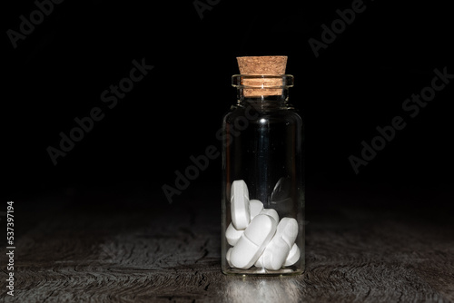 Glass bottle with white pills on a wooden table. the Container is located on a dark background.