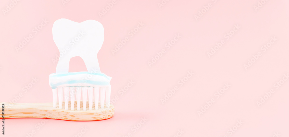 Bamboo toothbrush with toothpaste and paper tooth on the left on a soft pink Bamboo toothbrush with toothpaste and paper tooth on the left on a soft pink