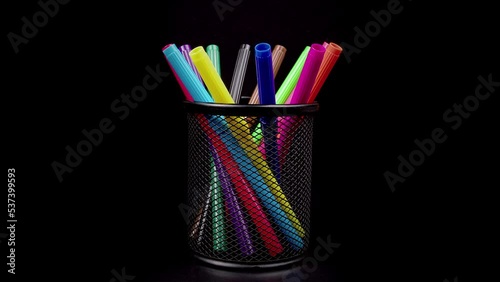 Colored pens in pencil case rotating in the isolated dark ,black background.