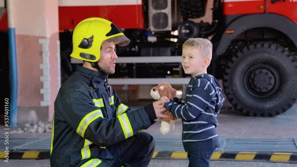 Little boy with firefighter in protective uniform in fire station Little boy with firefighter in protective uniform in fire station