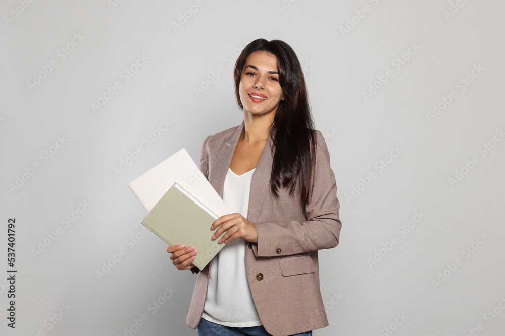 Happy young teacher with books on light grey background Happy young teacher with books on light grey background
