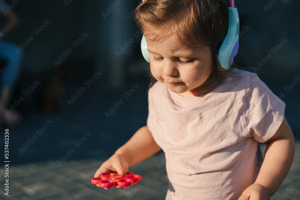 The baby girl spent time outside in the open air, wearing earplugs to keep from catching a cold. Toddler playing. Summer or autumn day The baby girl spent time outside in the open air, wearing earplugs to keep from catching a cold. Toddler playing. Summer or autumn day